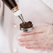 A person using an Ateco stainless steel flower nail to pipe chocolate frosting on a pastry.
