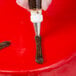 A hand holding an Ateco open star piping tip over a red cake.