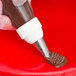 A hand using an Ateco leaf piping tip attached to a pastry bag to pipe chocolate frosting on a cake.