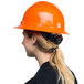 A woman wearing a Cordova Duo Safety orange full-brim hard hat with a ponytail.