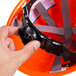 A hand holding a Cordova orange safety helmet with a black strap.