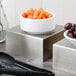 Two Tablecraft stainless steel square bowls, one with baby carrots and one with grapes.