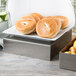 A Tablecraft rectangular stainless steel bowl with bagels on a plate on a counter.