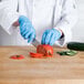 A person in blue gloves using a Choice chef knife to cut a tomato.