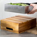 A hand holding a metal container with lettuce in a wood Tablecraft serving crate.