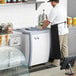 An Avantco ice cream dipping cabinet on a counter with a man in a white shirt and black apron.