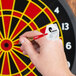 A hand holding a white Unicorn soft tip dart in front of a red and white dartboard.