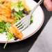 A Walco stainless steel salad fork holding a piece of salad on a plate.