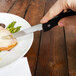 A person using a Walco steak knife to cut a piece of meat on a plate.