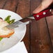 A hand holding a Walco steak knife cutting a piece of meat on a plate.