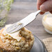 A person spreading butter on a muffin with a Walco stainless steel butter spreader.