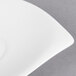 A Villeroy & Boch white porcelain saucer with a curved edge on a gray surface.