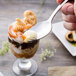 A hand holding a Walco stainless steel dessert spoon over a dessert in a glass.