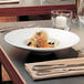 A Villeroy & Boch white porcelain pasta bowl filled with food on a set table with silverware.