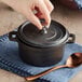 A hand using a spoon to lift the lid off a Valor pre-seasoned cast iron pot.