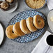 An Arcoroc Candour Azure oval platter with bagels and coffee on a table.
