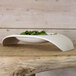 A Villeroy & Boch white porcelain bowl filled with green leaves on a wooden table.