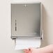 A person using a San Jamar True Fold Chrome paper towel dispenser on a wall.