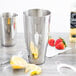 A silver Vollrath stainless steel cocktail shaker on a counter with lemons and strawberries.