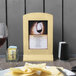 A Menu Solutions natural wood framed menu tent on a table with a glass of wine.