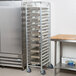 A Regency aluminum steam table pan rack filled with metal trays on wheels.