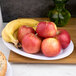 A Carlisle white oval melamine platter with apples and a banana on a table.