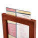 A Menu Solutions mahogany wood menu in a wooden holder on a table.