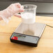 A hand holding a plastic container of white powder over a Taylor digital portion scale.