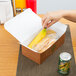 A hand putting a sandwich into a white Hearthstone take-out box.