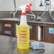 A yellow 32 oz. bottle of Noble Chemical Lemon Lance Disinfectant & Detergent Cleaner with purple text on a metal surface.