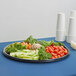 A WNA Comet black round catering tray with a plate of lettuce, carrots, and broccoli.
