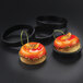 A group of round pastries with orange glaze and fruit on top in black Matfer Bourgeat tartlet rings.