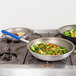 Two Vollrath Wear-Ever aluminum non-stick fry pans with vegetables cooking in one and a blue spatula in the other.