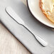 An Acopa Scottdale stainless steel butter spreader on a napkin next to a piece of bread with butter.