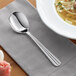 An Acopa Harmony stainless steel bouillon spoon on a napkin next to a bowl of soup.