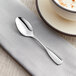 An Acopa Scottdale stainless steel demitasse spoon on a napkin next to a cup of coffee.