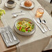 A table with a bowl of salad and silverware including Acopa Scottdale stainless steel bouillon spoons.
