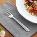 An Acopa Harmony stainless steel table fork on a napkin next to a plate of food.