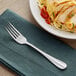 An Acopa Benson stainless steel dinner fork on a napkin next to a plate of spaghetti and chicken.