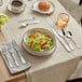 An Acopa Scottdale stainless steel dinner fork on a table with a bowl of salad.