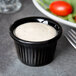 A black Tuxton fluted ramekin with white sauce in it.