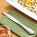 An Acopa Saxton stainless steel dinner knife on a napkin next to a plate of food.