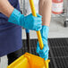 A person in Cordova blue latex rubber gloves with a yellow handle on a mop.