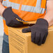 A person wearing Cordova brown jersey gloves and an orange safety vest holding a box.