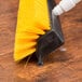 A black and yellow Carlisle Hi-Lo floor scrub brush on a wood surface.