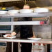 A chef using an Avantco high wattage strip warmer to plate food in a kitchen.