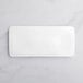 An Acopa bright white rectangular porcelain plate on a white marble surface.