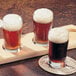 A wooden tray with four Libbey Esquire side water glasses filled with dark beer.