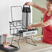 A woman in an apron using a Choice black wire 2 compartment airpot rack on a counter in a professional kitchen.