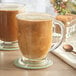 Two Acopa clear glass cafe mugs filled with coffee on a white surface with a spoon.